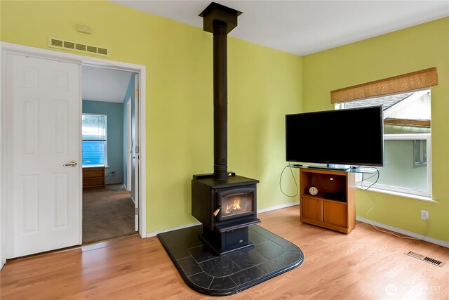 unfurnished living room featuring visible vents, a wood stove, and light wood finished floors