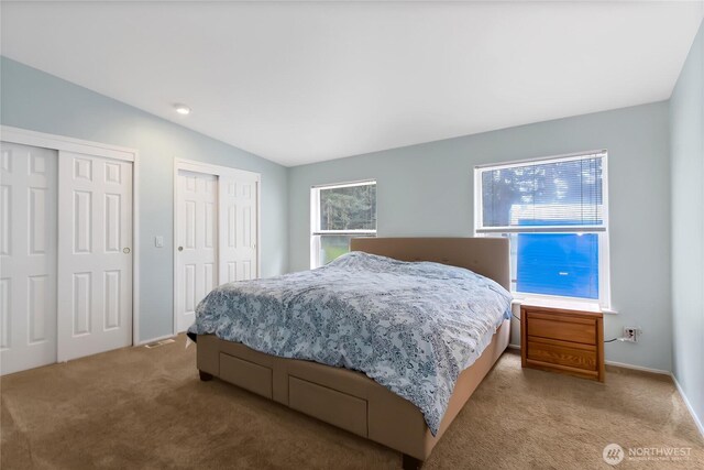bedroom featuring light carpet, two closets, and lofted ceiling