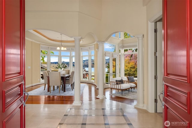 entryway featuring an inviting chandelier, decorative columns, a tray ceiling, crown molding, and baseboards