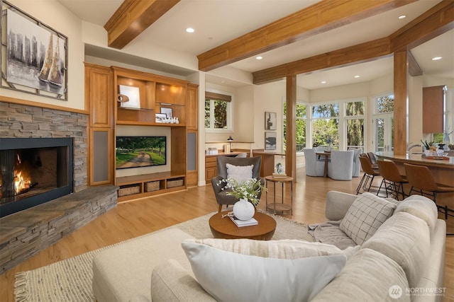 living room featuring a stone fireplace, recessed lighting, light wood finished floors, and beamed ceiling