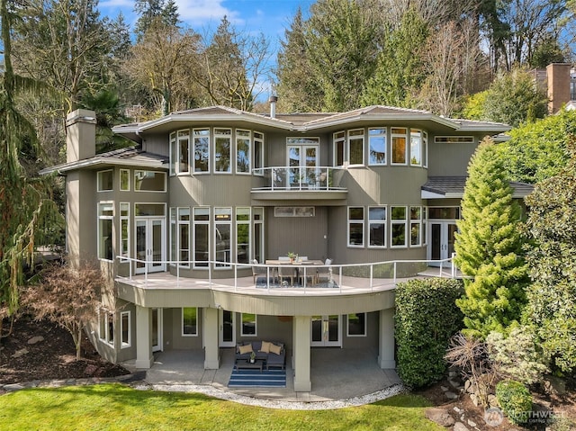rear view of house with a patio, a balcony, a chimney, an outdoor hangout area, and french doors