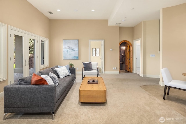 carpeted living area with visible vents, french doors, arched walkways, and baseboards