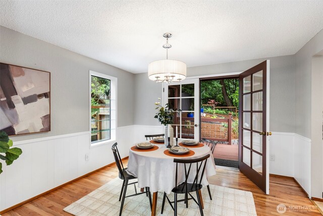 dining area with french doors, wainscoting, light wood-type flooring, and a notable chandelier