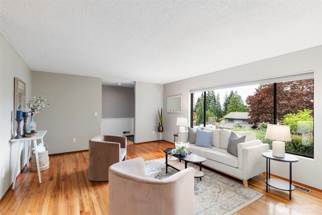 living room featuring a textured ceiling, visible vents, baseboards, and light wood-style floors