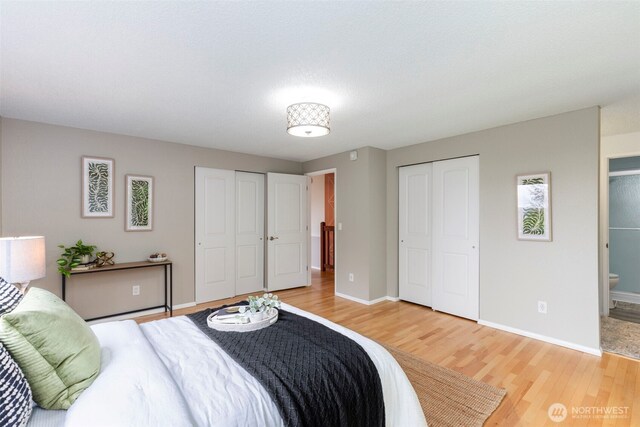 bedroom featuring baseboards, two closets, ensuite bath, and light wood-style flooring