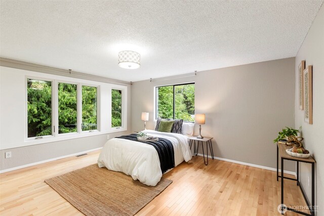 bedroom featuring baseboards, a textured ceiling, visible vents, and wood finished floors