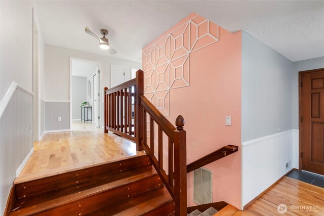staircase with visible vents, a textured ceiling, wood finished floors, and a wainscoted wall