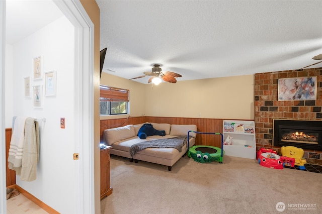 living room with light colored carpet, a brick fireplace, wainscoting, and ceiling fan