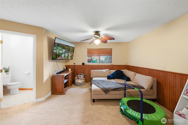 living room with carpet floors, wainscoting, wooden walls, a textured ceiling, and a ceiling fan