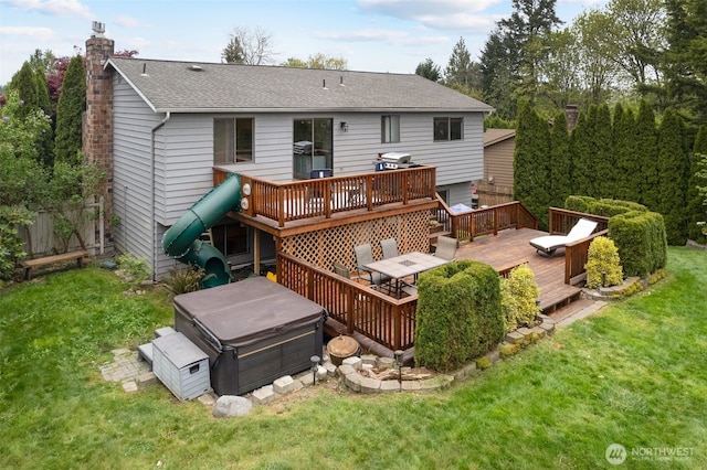 back of property with a chimney, roof with shingles, a lawn, a deck, and a hot tub