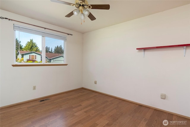 empty room with wood finished floors, a ceiling fan, visible vents, and baseboards