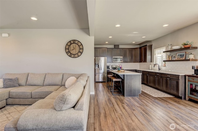 kitchen with a sink, dark brown cabinetry, open floor plan, and stainless steel appliances