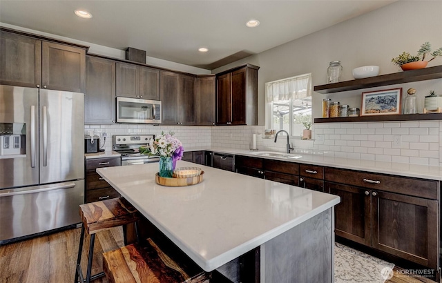 kitchen with open shelves, a sink, stainless steel appliances, light wood-type flooring, and a kitchen bar