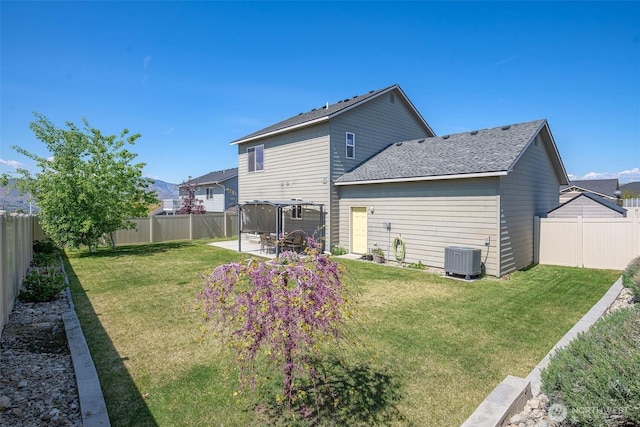 rear view of house with central air condition unit, a lawn, and a fenced backyard