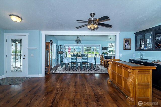 dining space with baseboards, ceiling fan, bar, and dark wood finished floors