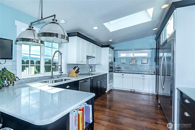 kitchen featuring white cabinets, light stone countertops, a sink, stainless steel appliances, and decorative backsplash