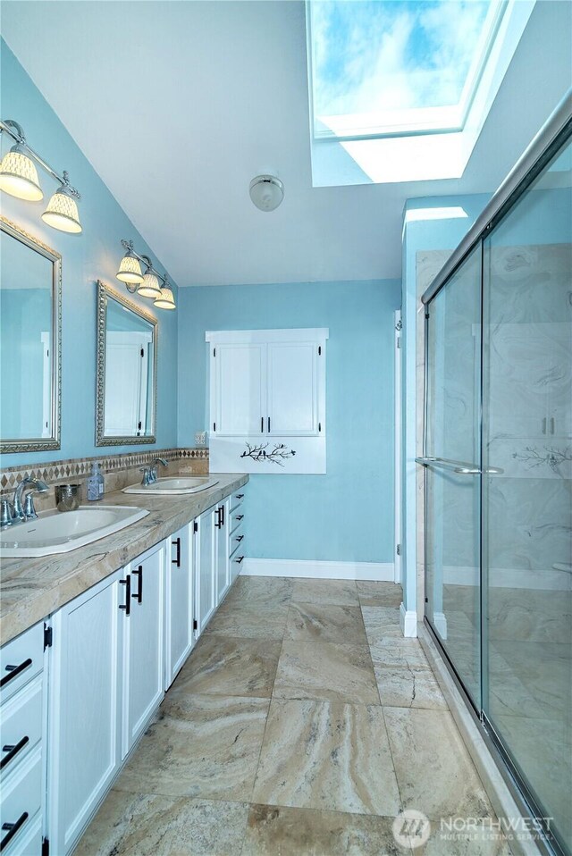 full bath featuring a skylight, double vanity, a shower stall, and a sink