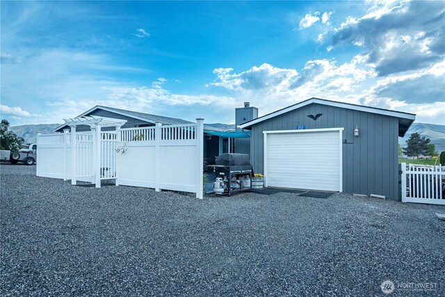 exterior space with fence, a chimney, an attached garage, and gravel driveway
