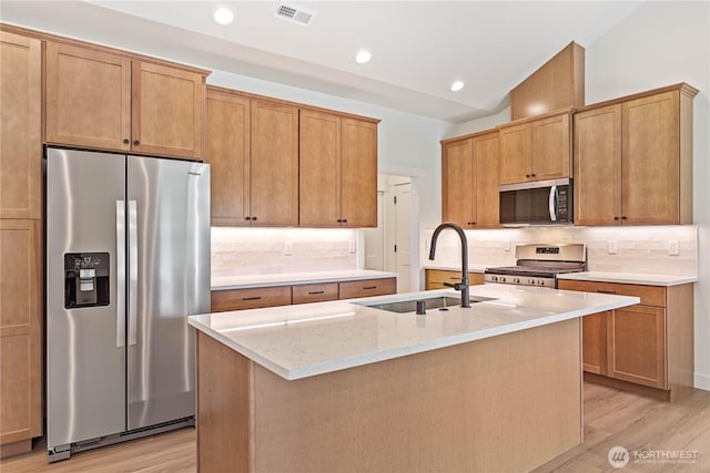 1200 E Georgia Ln, Everson, WA 98247 - kitchen featuring appliances with stainless steel finishes, light wood-style floors, decorative backsplash, light stone counters, and a kitchen island with sink