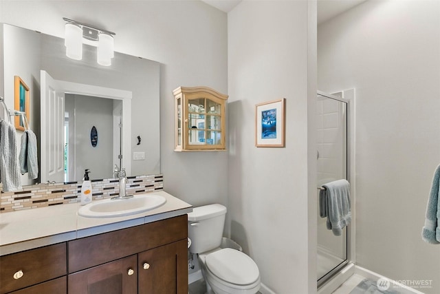 bathroom featuring toilet, vanity, a stall shower, and backsplash
