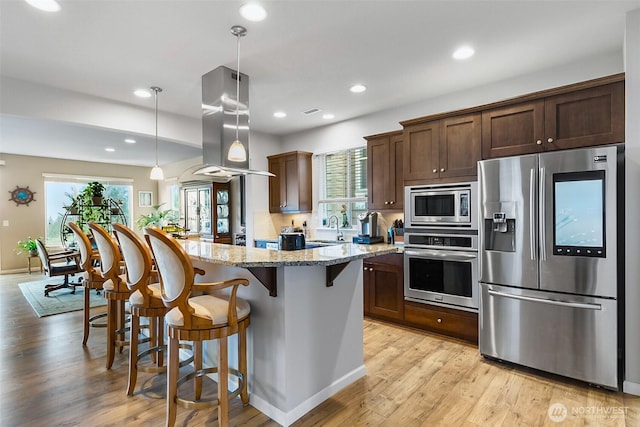 kitchen featuring light stone countertops, island range hood, plenty of natural light, a breakfast bar area, and appliances with stainless steel finishes