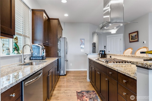 kitchen featuring island range hood, appliances with stainless steel finishes, dark brown cabinets, light wood finished floors, and a sink