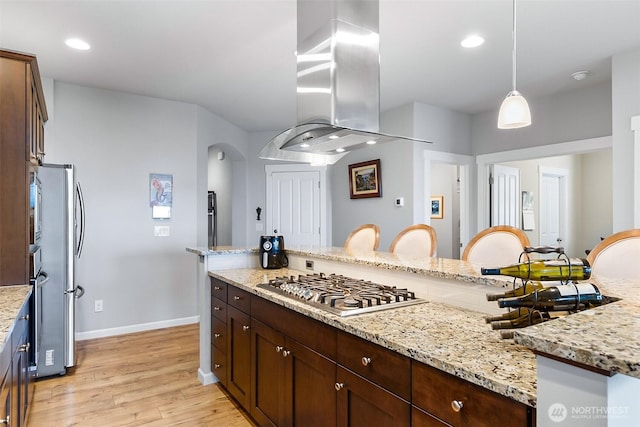 kitchen with appliances with stainless steel finishes, light wood finished floors, island exhaust hood, baseboards, and pendant lighting