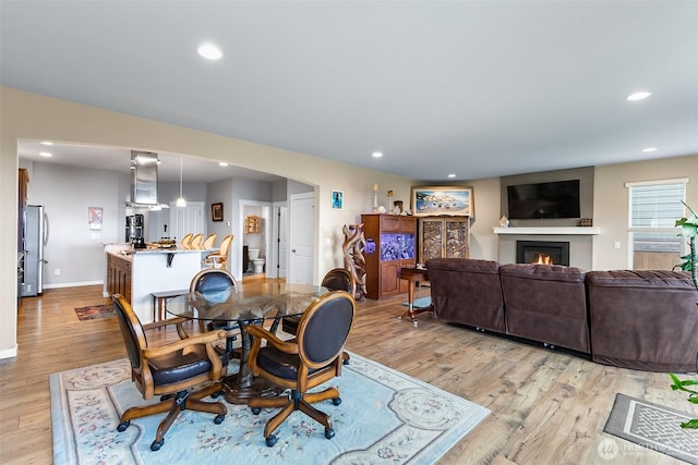 dining area featuring recessed lighting, light wood-style flooring, and a glass covered fireplace