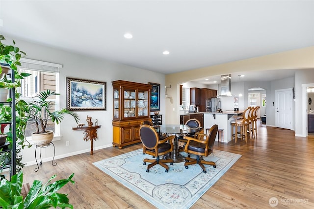 dining room with arched walkways, light wood finished floors, and plenty of natural light