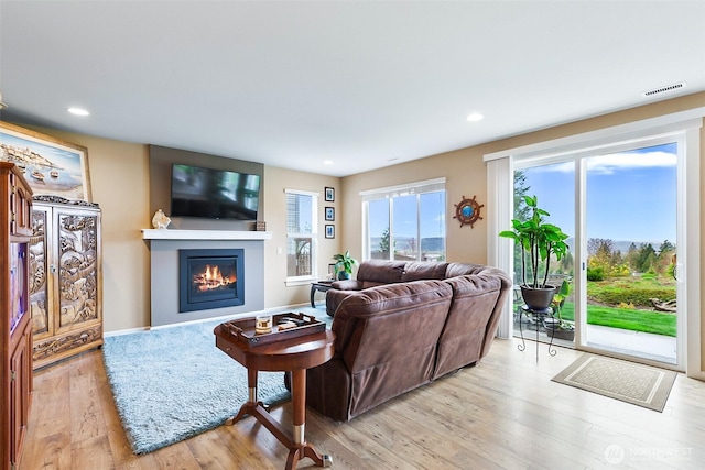 living area featuring visible vents, wood finished floors, recessed lighting, and a glass covered fireplace