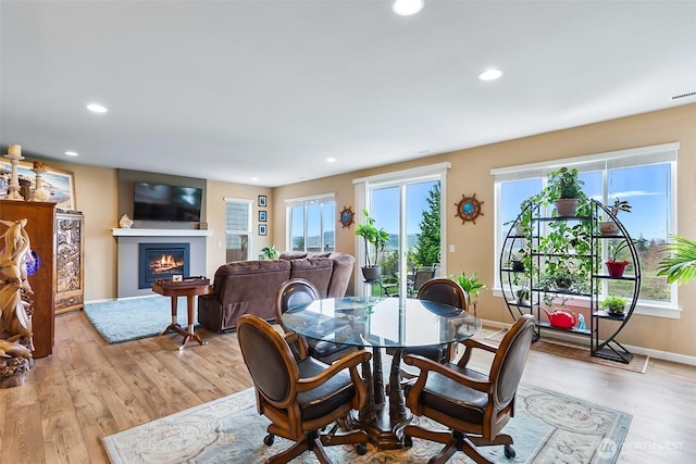 dining space with a glass covered fireplace, light wood-style floors, recessed lighting, and baseboards