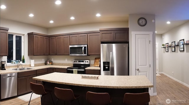 kitchen with dark brown cabinets, appliances with stainless steel finishes, light countertops, light wood-style flooring, and a kitchen bar