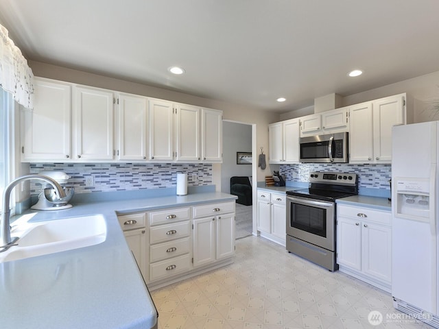 kitchen featuring appliances with stainless steel finishes, a sink, light countertops, white cabinetry, and backsplash