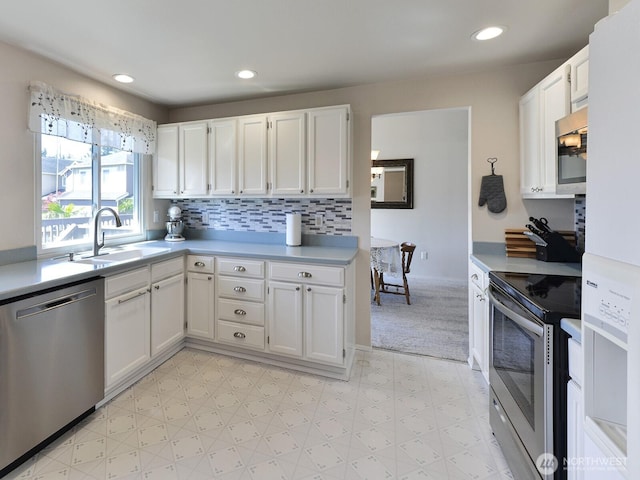 kitchen with a sink, light countertops, light floors, stainless steel appliances, and white cabinetry