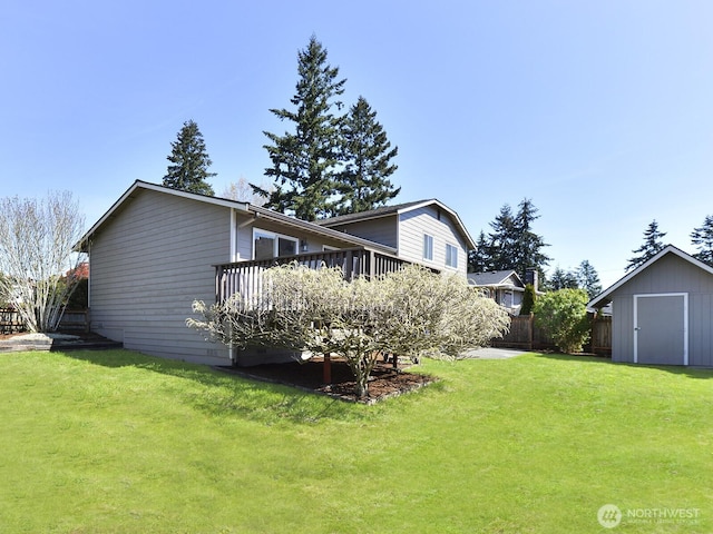 rear view of property featuring fence, a storage unit, a wooden deck, a lawn, and an outdoor structure