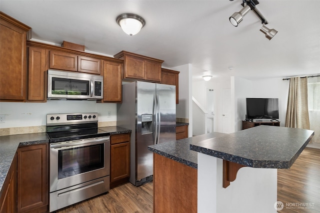 kitchen with a kitchen breakfast bar, dark countertops, a center island, dark wood finished floors, and stainless steel appliances