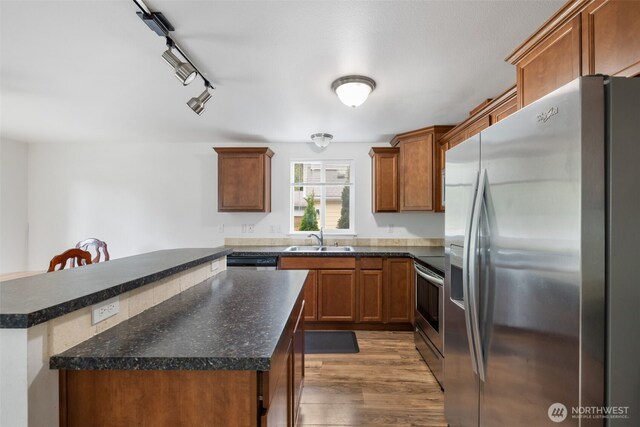 kitchen with dark wood-style flooring, dark countertops, a center island, a sink, and appliances with stainless steel finishes