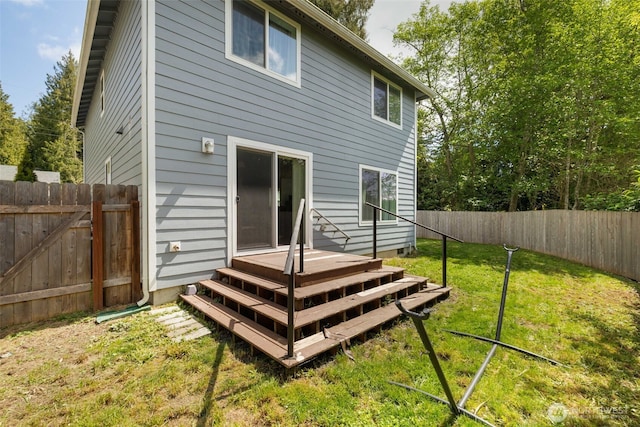 rear view of house featuring a fenced backyard, a wooden deck, and a lawn