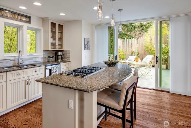 kitchen featuring decorative backsplash, a kitchen bar, stainless steel gas cooktop, a sink, and glass insert cabinets