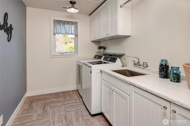 washroom featuring visible vents, baseboards, washing machine and clothes dryer, a sink, and cabinet space