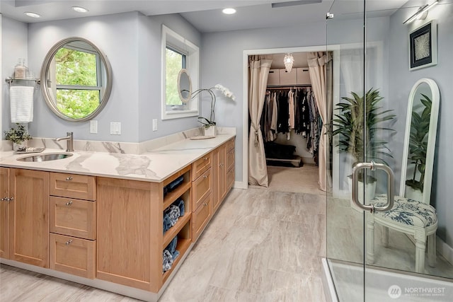 bathroom with double vanity, a shower with door, a sink, and a walk in closet