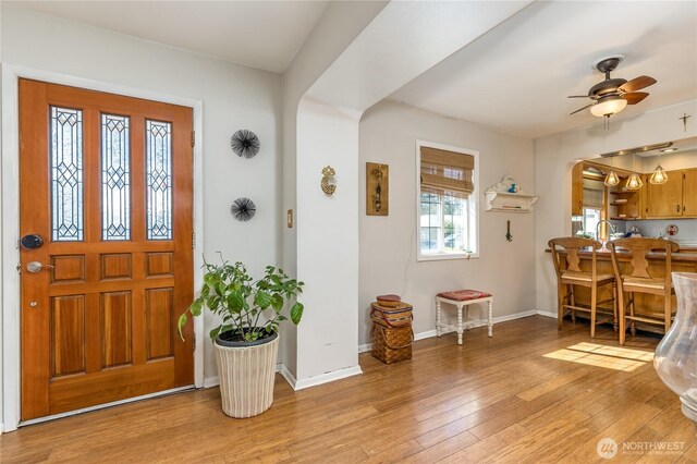 foyer with arched walkways, baseboards, a ceiling fan, and light wood finished floors