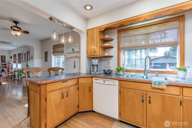 kitchen with a peninsula, ceiling fan, a sink, light wood finished floors, and dishwasher