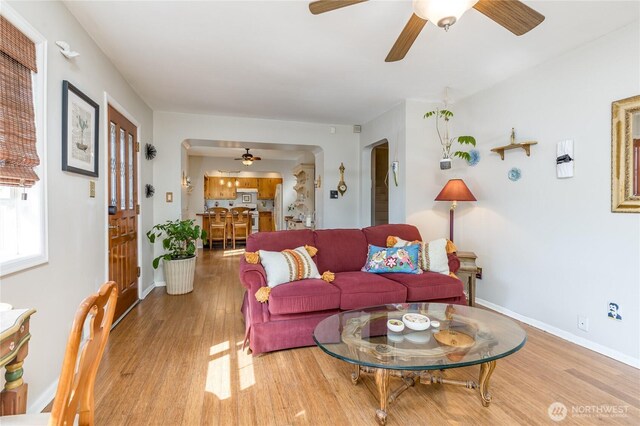 living area featuring arched walkways, baseboards, a ceiling fan, and wood finished floors