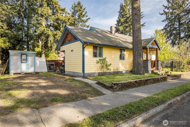 view of side of home with a shingled roof, an outdoor structure, a chimney, and a yard