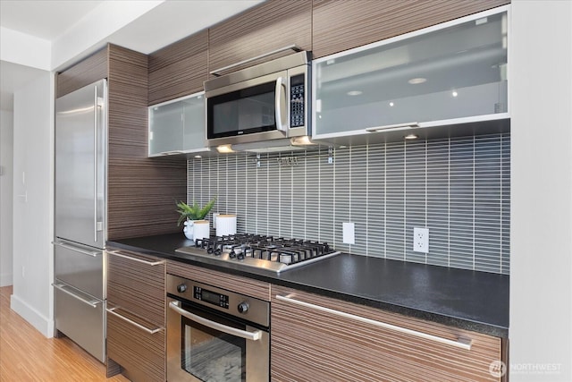 820 Blanchard St Unit 1507, Seattle, WA 98121 - kitchen with brown cabinetry, dark countertops, modern cabinets, backsplash, and stainless steel appliances