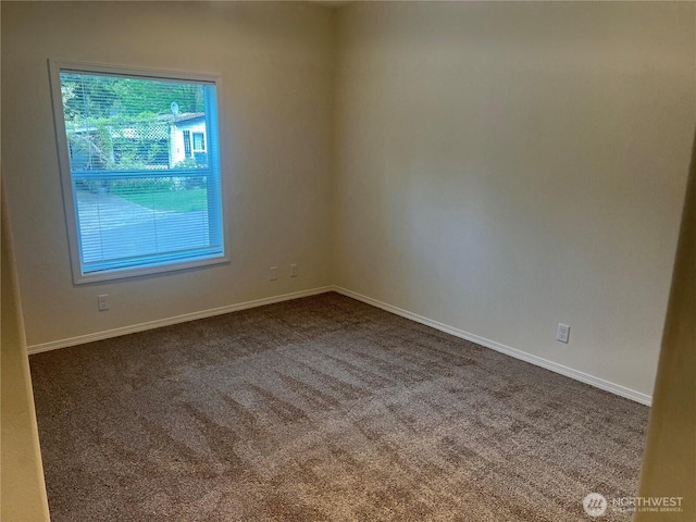 unfurnished room featuring dark colored carpet and baseboards