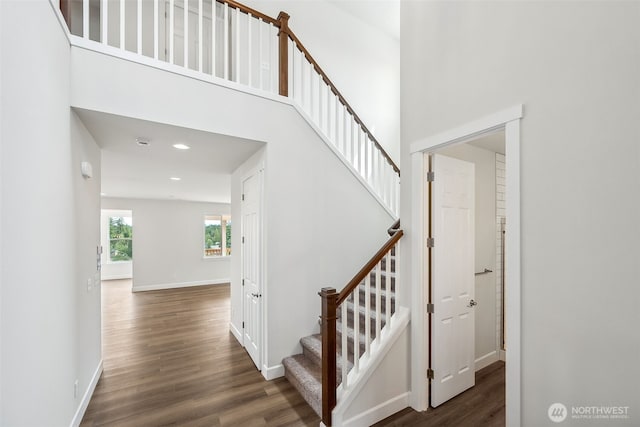 stairs with recessed lighting, baseboards, wood finished floors, and a towering ceiling