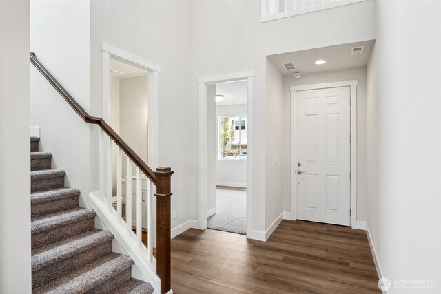 foyer entrance featuring visible vents, wood finished floors, stairway, baseboards, and a high ceiling