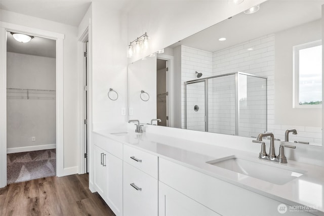 bathroom featuring a sink, a stall shower, wood finished floors, and a spacious closet